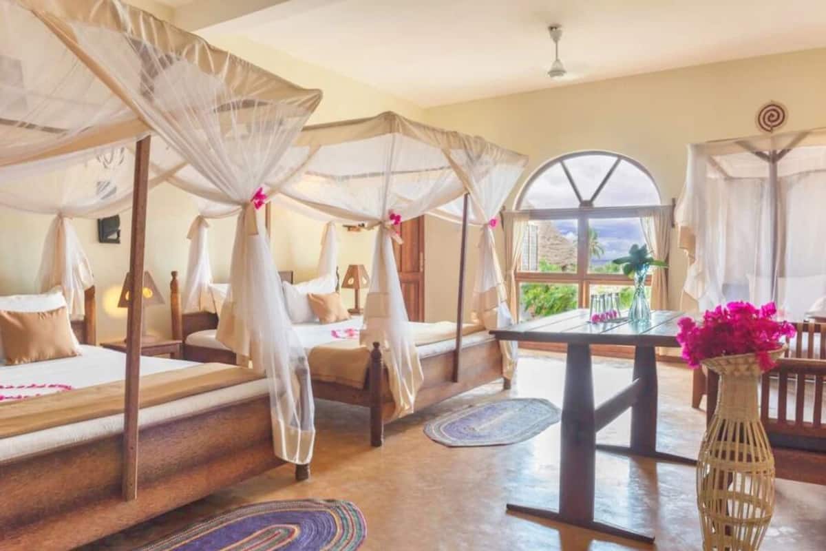 Una habitación con una cama bajo un dosel, una mesa con un florero y vistas a través de una ventana.