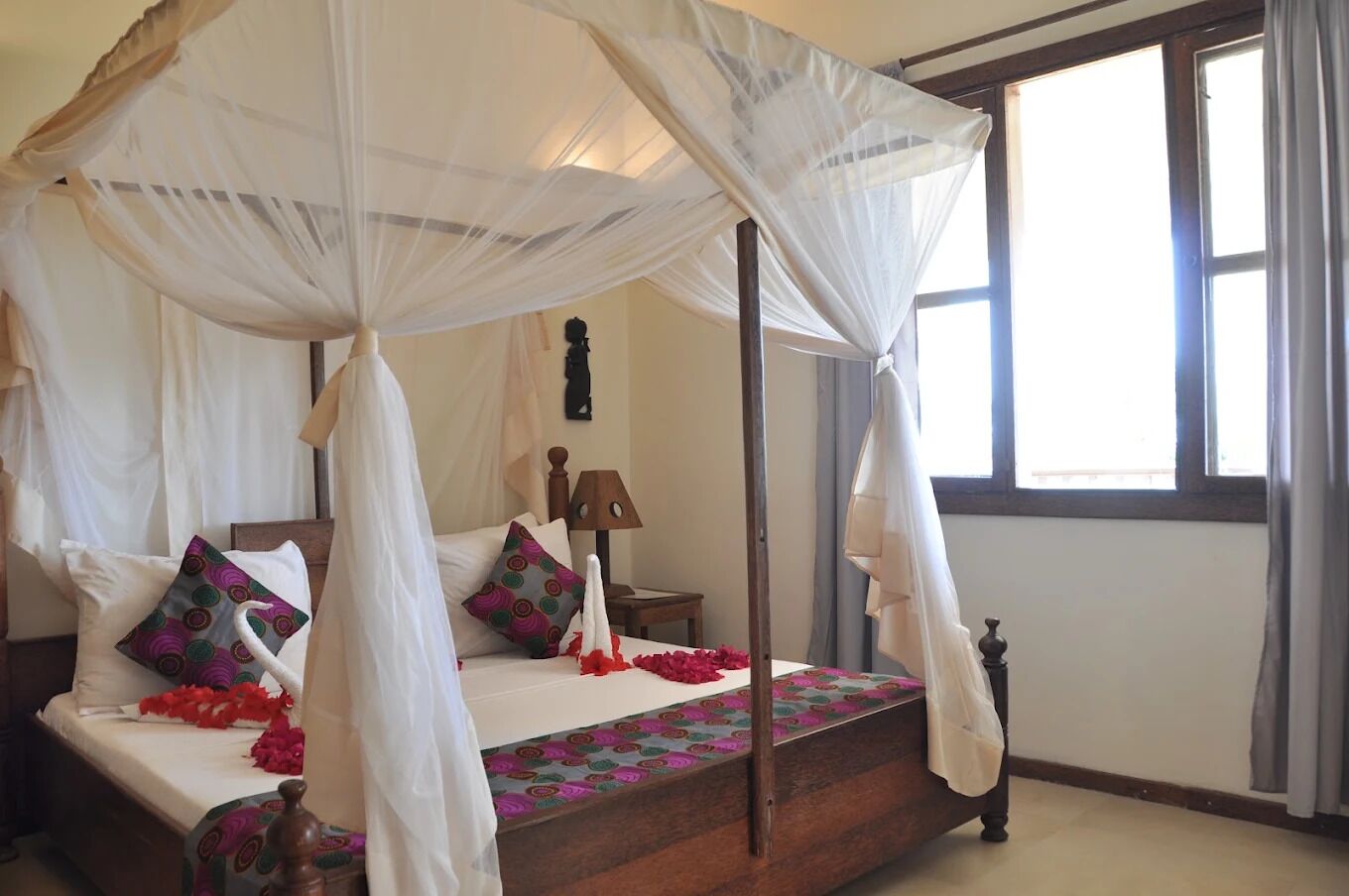 Una cama con dosel sostenido por cuatro postes, con estructura de madera, un edredón estampado y una ventana con cortinas.