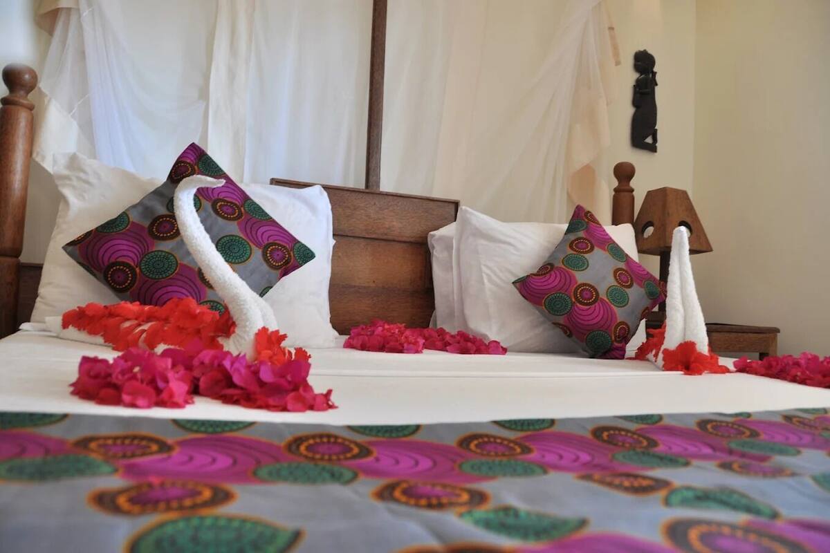 Una cama con una colcha colorida, almohadas blancas con un diseño circular y flores rojas.