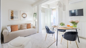 A modern living room with a sofa, a dining table set for two, and a TV mounted on the wall. - The Sunwall Loft in Lucca (Lucca)