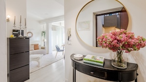 A modern living room with a dark wood console, a white sofa, a round mirror, and a vase with pink flowers. - The Sunwall Loft in Lucca (Lucca)