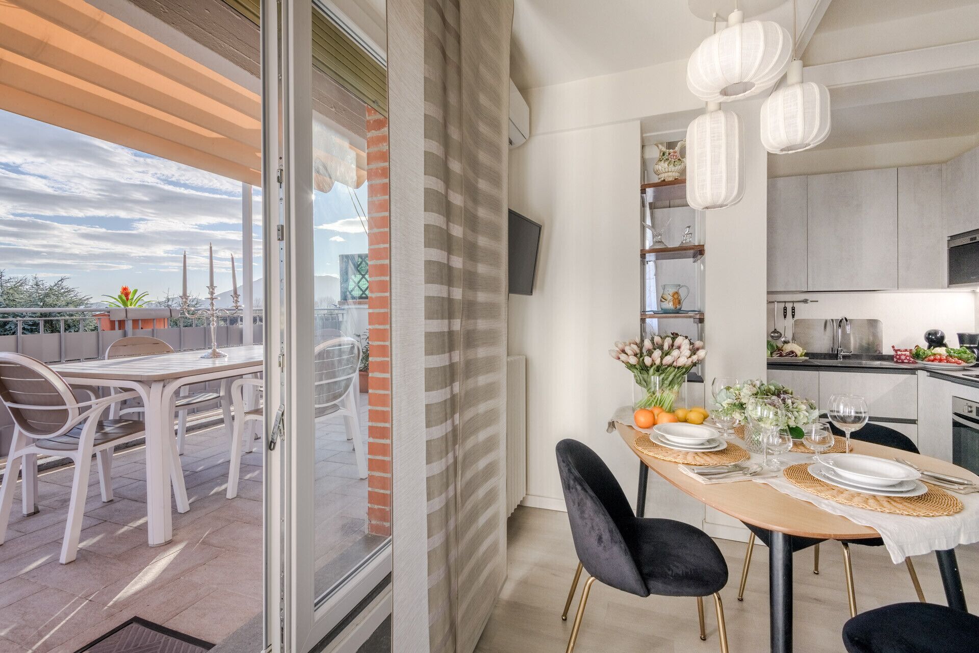 Un coin repas avec une table dressée pour deux personnes, une cuisine en arrière-plan et une vue sur le paysage urbain à travers une porte vitrée.