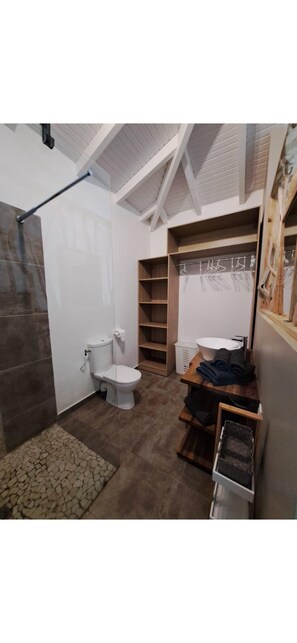 Un bagno con doccia, toilette, lavandino e mensole in legno.