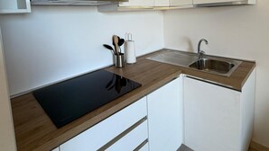 Et moderne køkken med hvide skabe, en sort bordplade, en rustfri stålvask og en integreret emhætte.