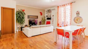 A living room with a white sofa, a TV, and a dining area with a white table and orange chairs. - Elegant and quiet little gem in downtown milan (M4 DATEO) (Milano)