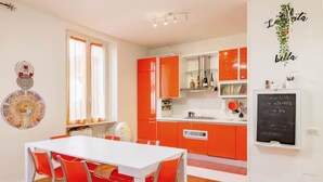 A modern kitchen with orange cabinets, a white dining table with red chairs, and a chalkboard with writing. - Elegant and quiet little gem in downtown milan (M4 DATEO) (Milano)