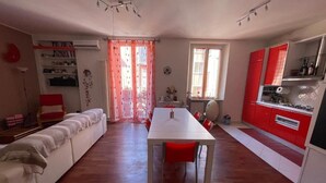 A spacious living area with a long white table and red chairs, a white sofa, and a kitchen area with red cabinets. - Elegant and quiet little gem in downtown milan (M4 DATEO) (Milano)