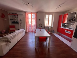 A spacious living area with a long white table and red chairs, a white sofa, and a kitchen area with red cabinets. - Elegant and quiet little gem in downtown milan (M4 DATEO) (Milano)