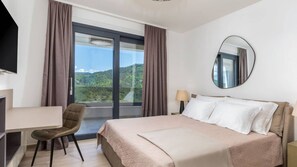 A hotel room with a large bed, a desk, a chair, a round mirror, and a view of a mountainous landscape through the window. - Butoniga Hills by Villas Guide (Pazin)