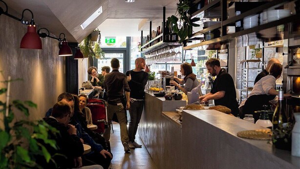 A busy restaurant with a long counter, customers seated, and staff serving. - Chorlton Garden Rooms - Relax, work, stay & play. (Manchester)