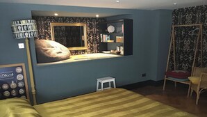A bedroom with a bed, a small stool, a chair, a mirror, and a shelf with books and decorative items. - Chorlton Garden Rooms - Relax, work, stay & play. (Manchester)