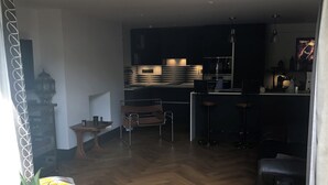 A modern kitchen with dark cabinetry and a central island, a dining area with a wooden table and chairs, and a living space with a sofa and a coffee table. - Chorlton Garden Rooms - Relax, work, stay & play. (Manchester)