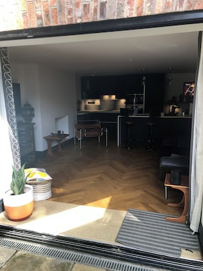 A modern kitchen with dark cabinetry and a central island, a dining area with a wooden table and chairs, and a living space with a sofa and a coffee table. - Chorlton Garden Rooms - Relax, work, stay & play. (Manchester)