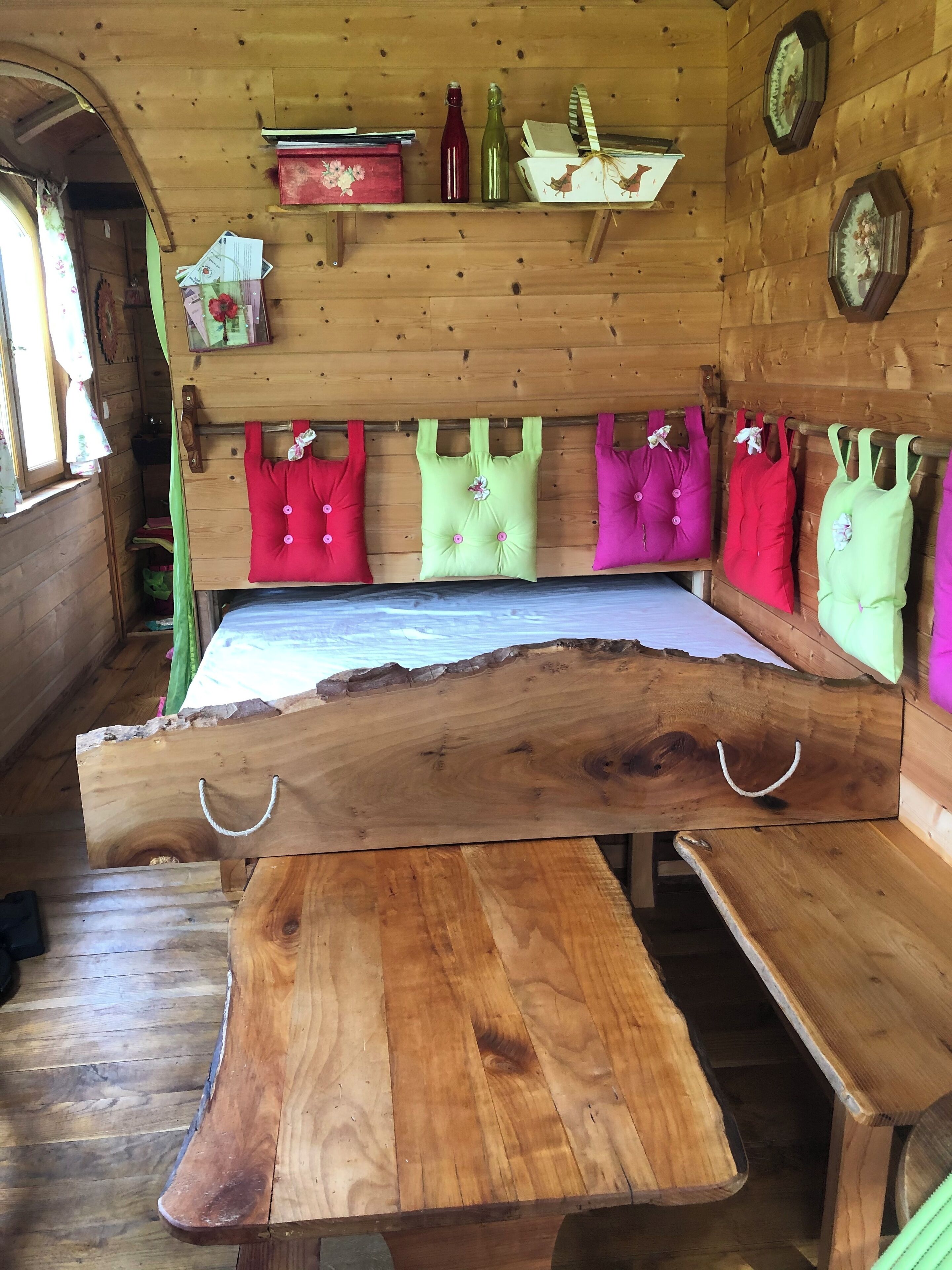 A wooden interior with a bench, pillows, and a shelf with bottles and books.