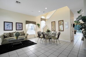 Ein geräumiges Wohnzimmer mit Sofa, Couchtisch, Esstisch und Stühlen. An den Wänden befinden sich gerahmte Bilder und eine Treppe, die zu einer weiteren Ebene führt.