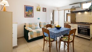 Un espacio habitable compacto con sofá, mesa de comedor, sillas, zona de cocina con horno y aire acondicionado de pared.