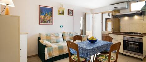 Un espacio habitable compacto con sofá, mesa de comedor, sillas, zona de cocina con horno y aire acondicionado de pared.