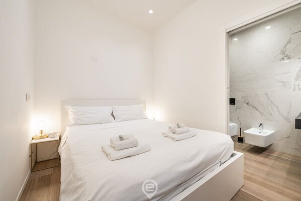 A modern hotel room with a large bed, a bedside table, a nightstand, a bathroom with a marble wall, and a sink. - Loft 2 Via Campidano - Modern studio for your stay (Cagliari)
