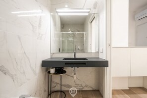 Ein modernes Badezimmer mit Marmorwand, einem schwarzen Waschbecken und einer Duschkabine aus Glas.