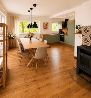 Eine geräumige Küche mit Holztisch, Stühlen, Pendelleuchten und Blick ins Freie.