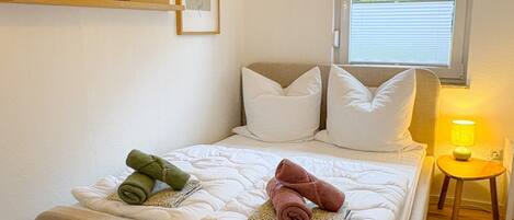 A bedroom with a bed, pillows, a bedside lamp, a window, and wall-mounted artwork.