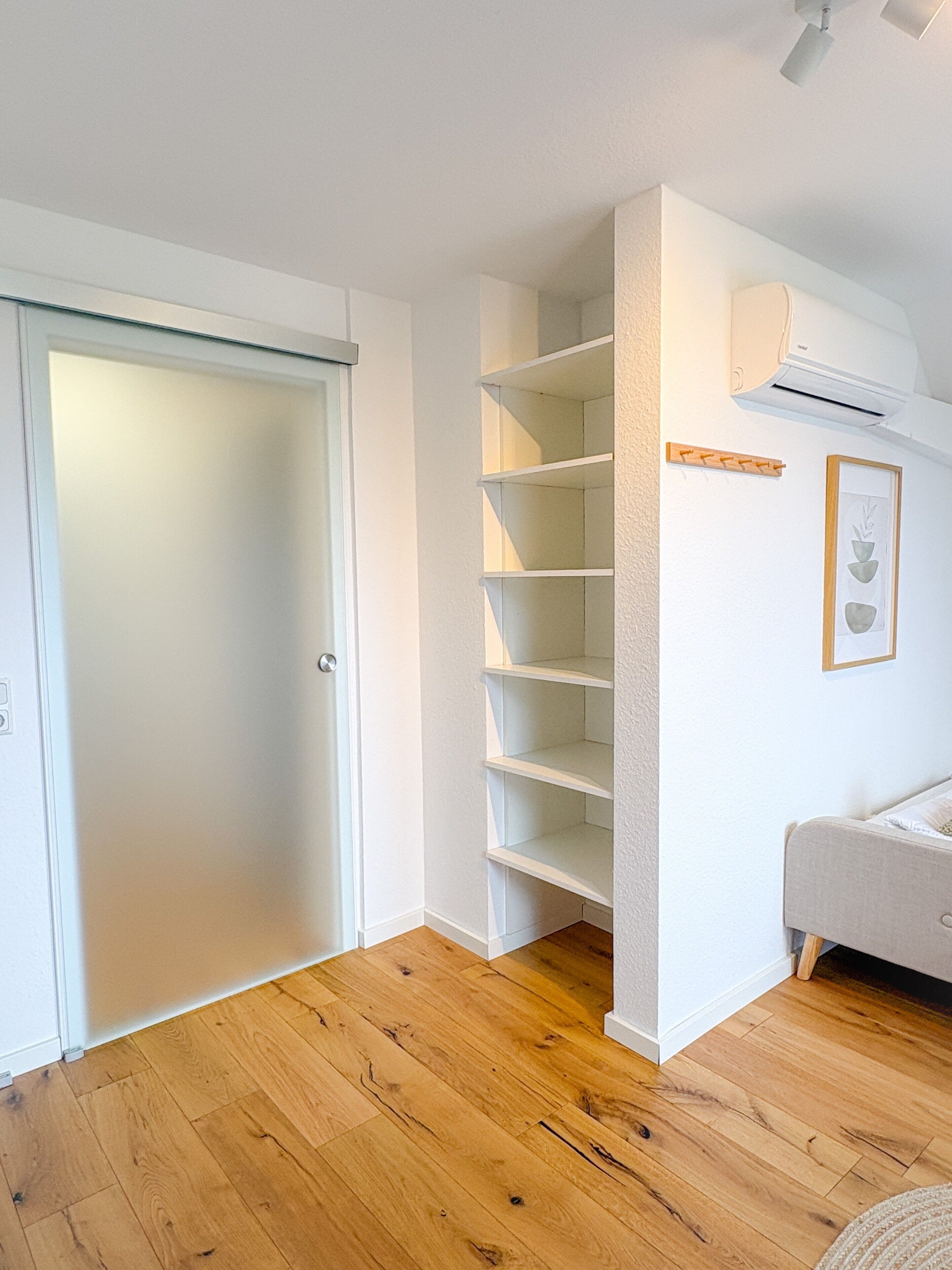 Ein Zimmer mit Holzboden, einer weißen Tür, einer eingebauten Regaleinheit und einer weißen Klimaanlage an der Wand.