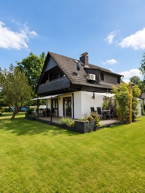 Ein zweistöckiges Haus mit Balkon, überdachter Terrasse und gepflegtem Rasen.