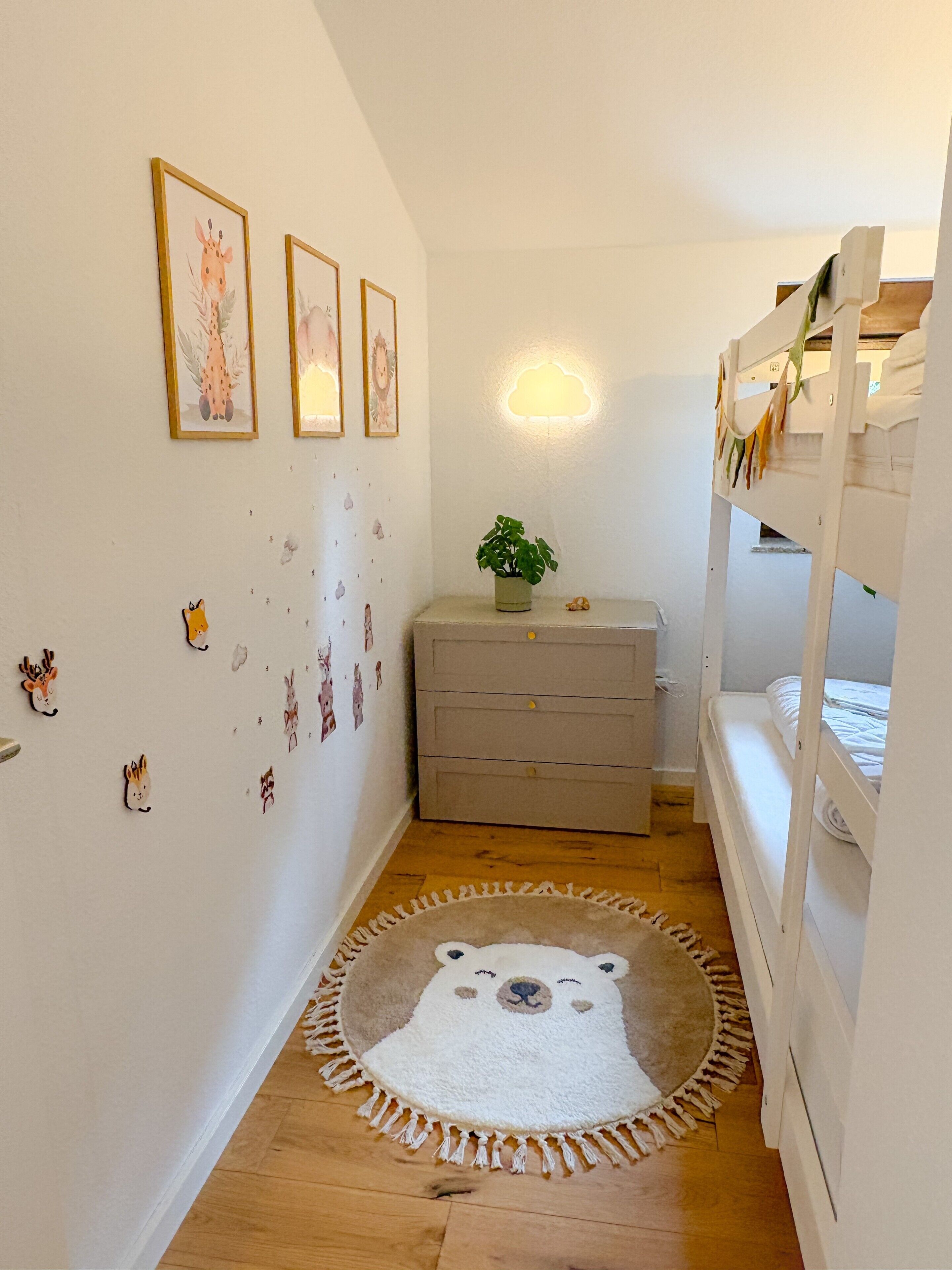 Ein Kinderzimmer mit Etagenbett, Kommode, Wanddekorationen und Teppich.