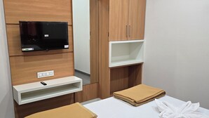 A hotel room with a bed, a TV mounted on the wall, a wooden wardrobe, and a small shelf. - Hotel Sagar Family Lodge (Man)
