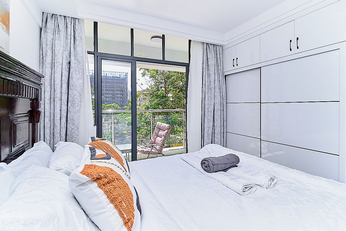 A hotel room with a large bed, a chair by the window, and a wardrobe.