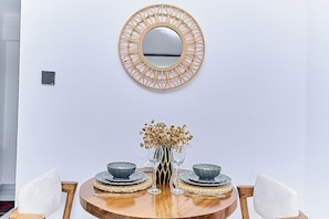 Ein Essbereich mit einem runden Holztisch, zwei Stühlen, einer Vase mit goldenen Blumen und einem an der Wand befestigten Spiegel.