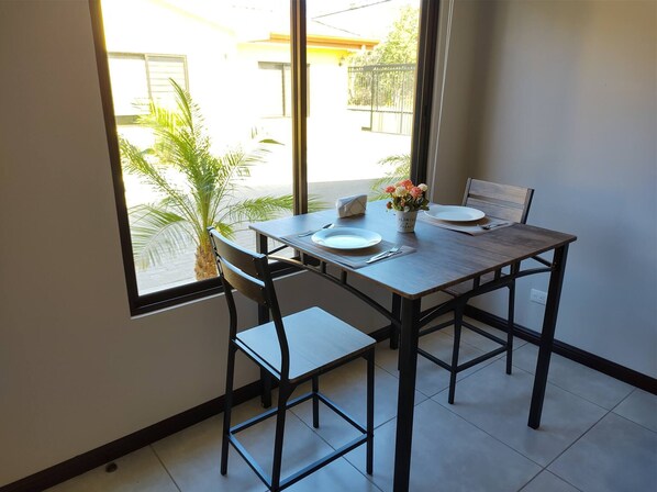 A dining area with a table, chairs, and a window with a view of a building and greenery outside. - #1 New & Modern 2 bed Suite With Shared Pool (Liberia)