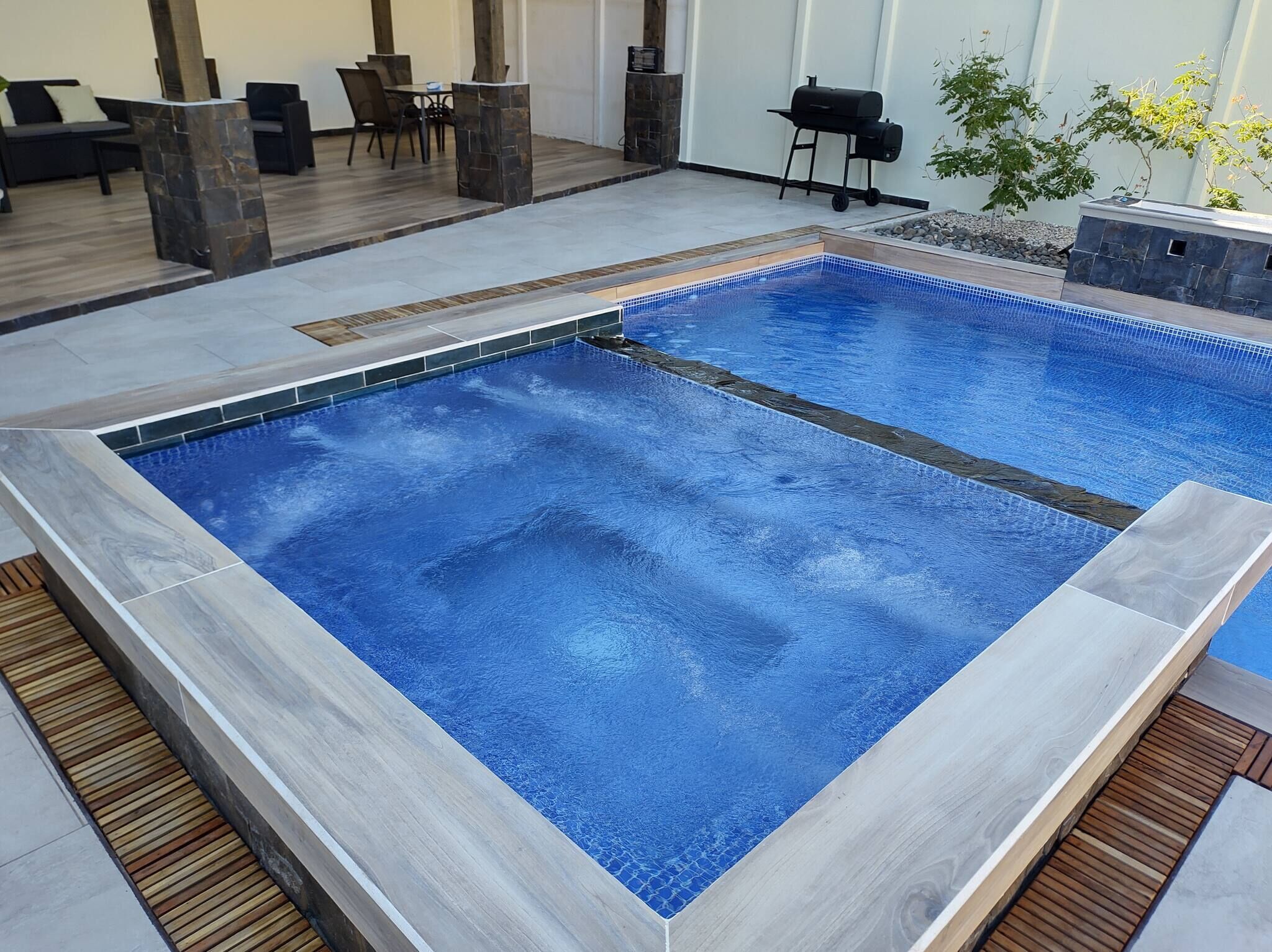 A rectangular indoor pool with a tiled edge, surrounded by a wooden deck and stone pillars.