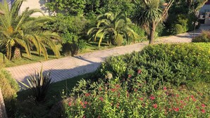 A garden pathway leading to a building with a red-tiled roof, surrounded by lush greenery and palm trees. - Luxury villa with amazing views in 3200m2 (Laroque-des-Albères)