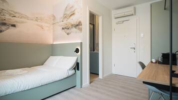 Un dormitorio moderno con una cama individual, una mesa de comedor de madera y una cocina visible a través de una puerta abierta.