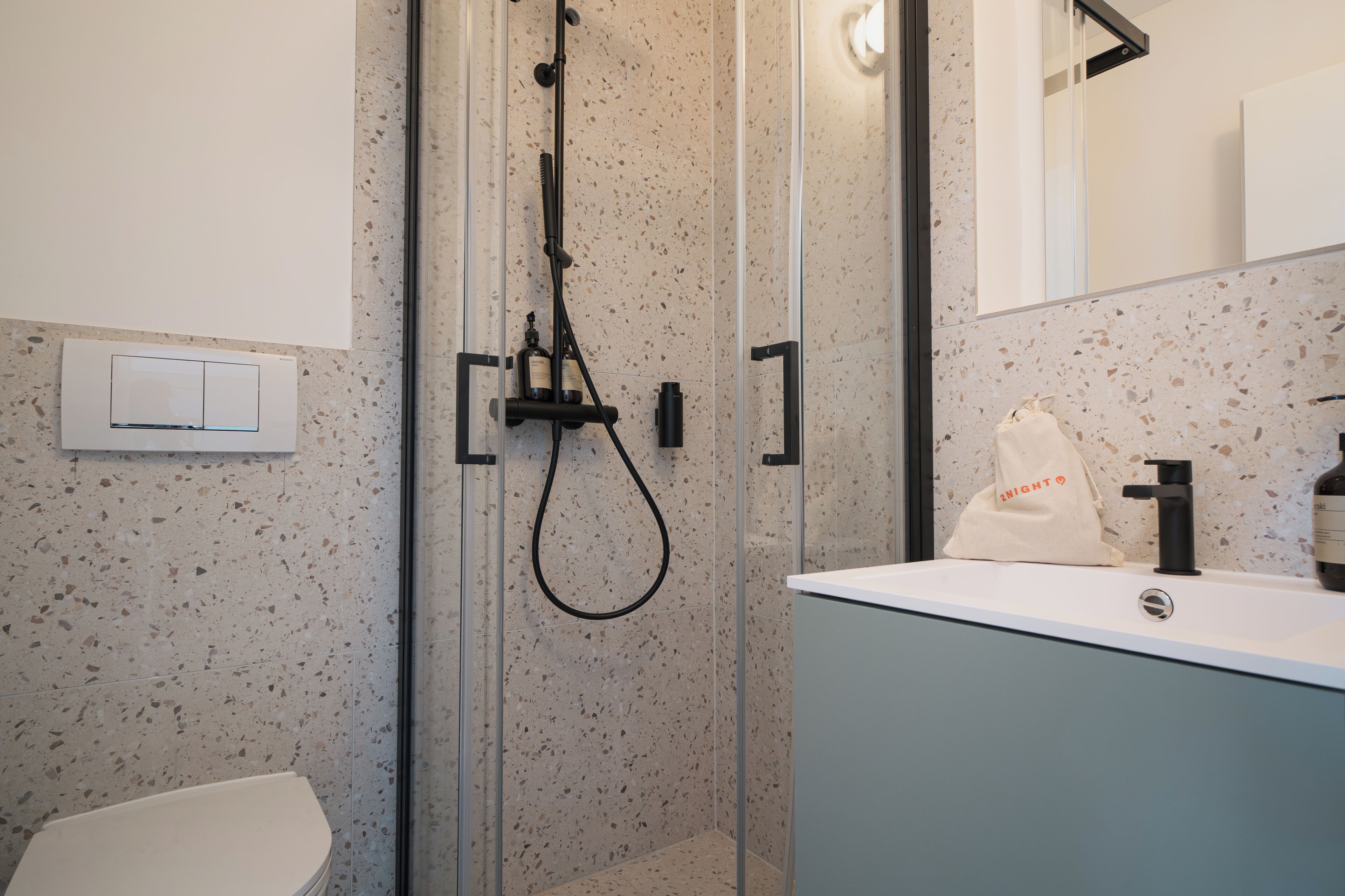 A modern bathroom with a shower enclosure, a toilet, and a sink with a mirror.