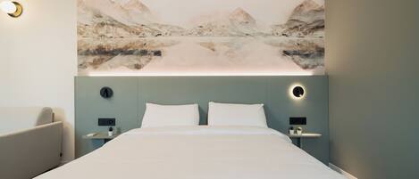 Una habitación de hotel moderna con una cama grande, dos mesitas de noche y una obra de arte en la pared que representa un paisaje montañoso.