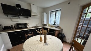 A compact kitchen with a dining table, a built-in oven, and a window with curtains. - Charming Cottage in a Converted Farmhouse with Wi-Fi (Vendin-le-Vieil)