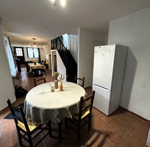A dining area with a round table, chairs, a white refrigerator, and a staircase. - Charming Cottage in a Converted Farmhouse with Wi-Fi (Vendin-le-Vieil)