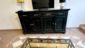A black TV stand with a flat-screen TV, a lamp, and a patterned rug. - Charming Cottage in a Converted Farmhouse with Wi-Fi (Vendin-le-Vieil)