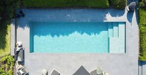 Une piscine rectangulaire bordée de carreaux, entourée de chaises longues et d’un petit espace salon.