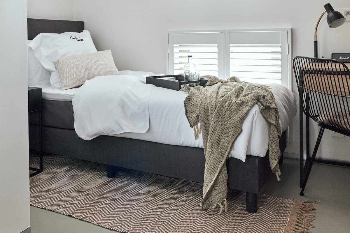 A bedroom with a bed, a desk, a chair, a lamp, and a window.