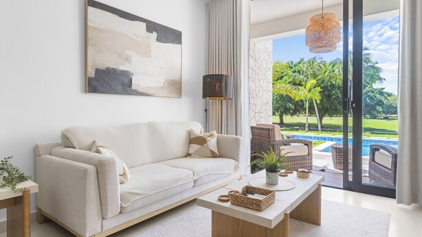 A modern living room with a sofa, coffee table, and a view of a swimming pool and greenery. - Cocotal Beach Homes Punta Cana (Punta Cana)