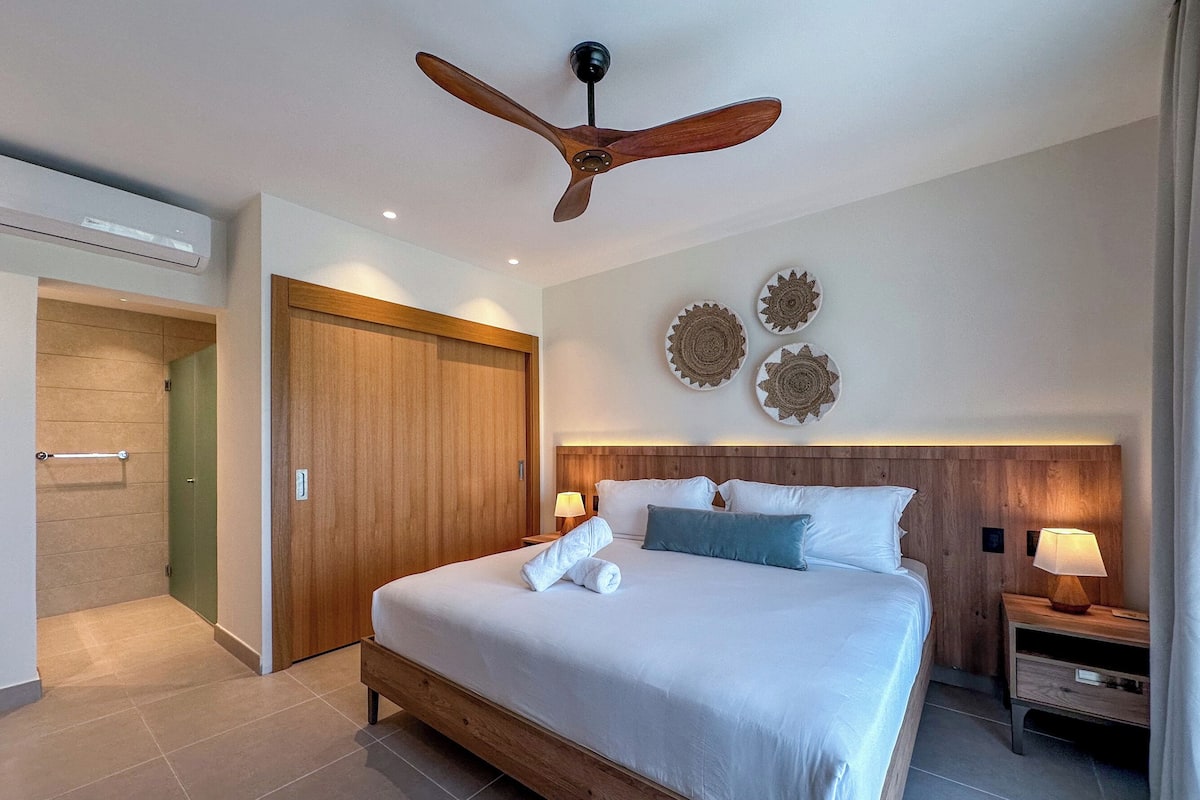 A hotel room with a wooden bed, a ceiling fan, and decorative wall art.