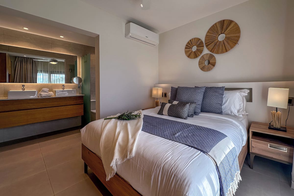 A modern bedroom with a large bed, two bedside tables with lamps, a vanity with a mirror, and decorative wall art.