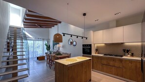 A modern kitchen with wooden cabinets, a central island, and a dining area with a staircase. - Cocotal Beach Homes Punta Cana (Punta Cana)