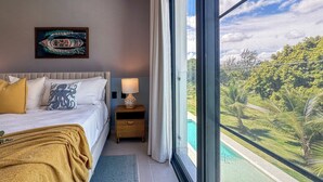 A bedroom with a bed, nightstand, and a view of a swimming pool and greenery. - Cocotal Beach Homes Punta Cana (Punta Cana)
