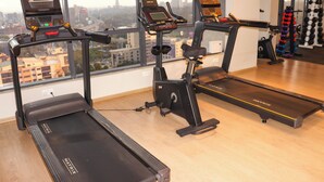 Three treadmills in a gym with a city view through large windows. - Elite Residence 1 BR: Balcony, Heated Pool, Power backup, Sky Gym& 24/7 Security (Nairobi)