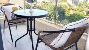 A balcony with wicker chairs, a small round table, and a vase with flowers. - Elite Residence 1 BR: Balcony, Heated Pool, Power backup, Sky Gym& 24/7 Security (Nairobi)