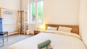 Une chambre à coucher avec un lit, une échelle en bois, une chaise, une table de chevet et une fenêtre.
